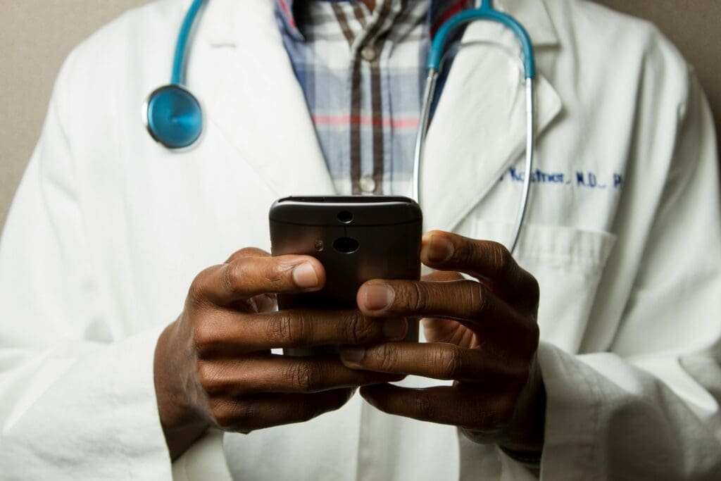 person wearing white coat with green stethoscope on neck using phone while standing