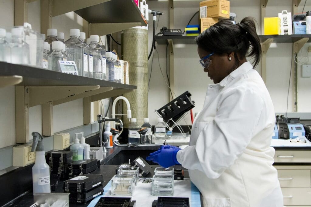 a black woman doctor standing in front of a microscope doing medical research