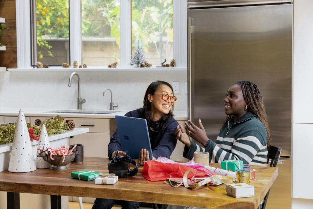 a Black woman sitting at a table in front of a window with a friend. they are smiling and talking