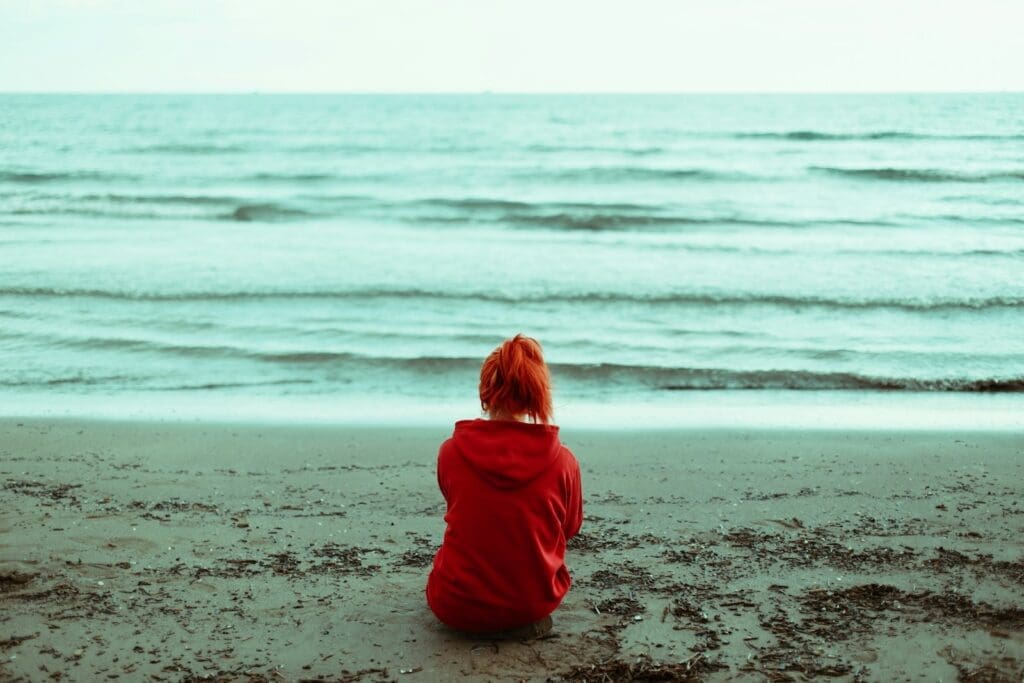 a person sitting alone on a beach. grief can make you feel isolated