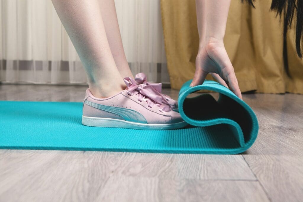 person wearing pink nike sneakers is unrolling a teal yoga mat for exercise on her GLP 1 journey
