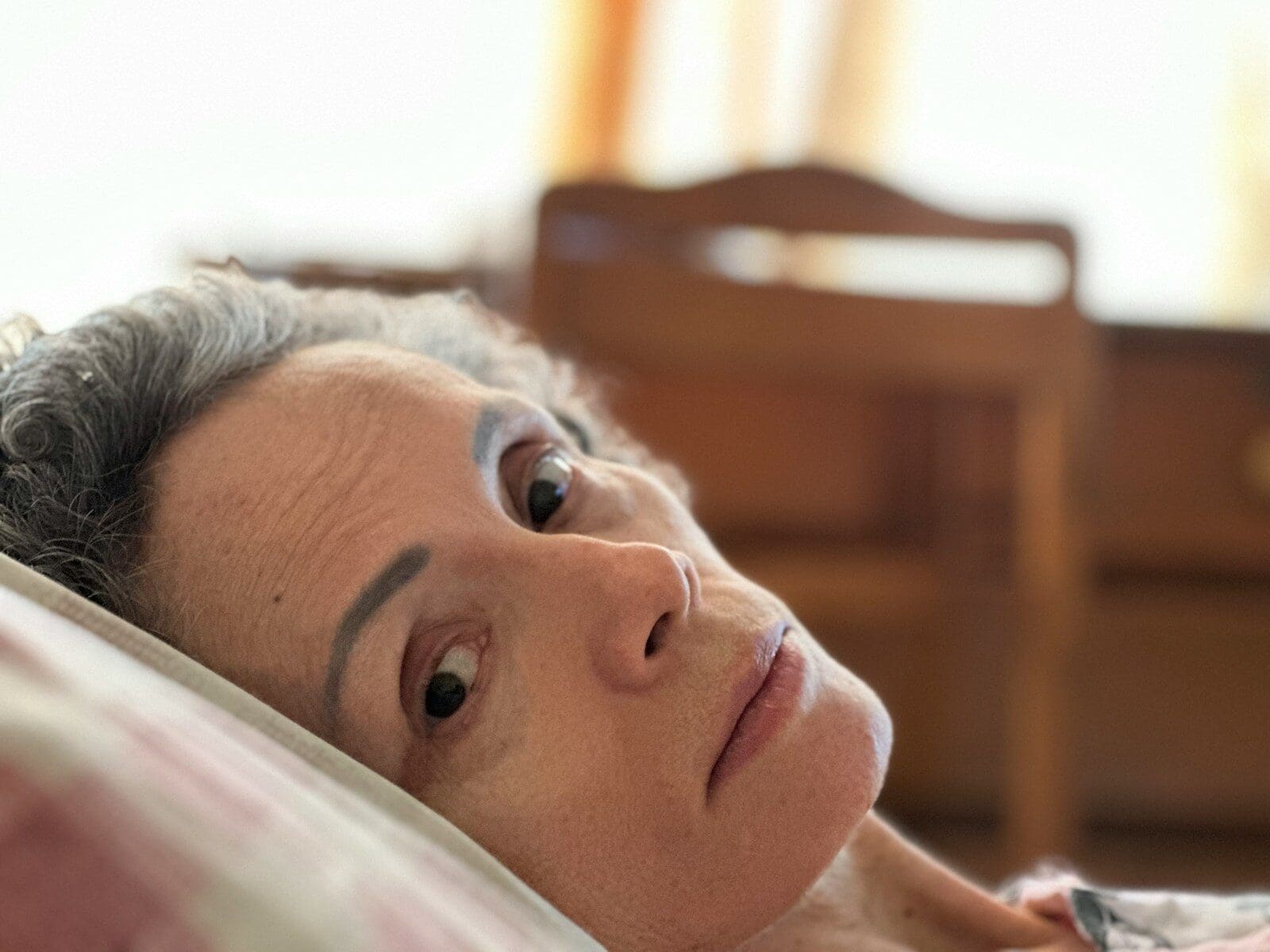 a white woman laying on a bed with her eyes open, she seems worried.