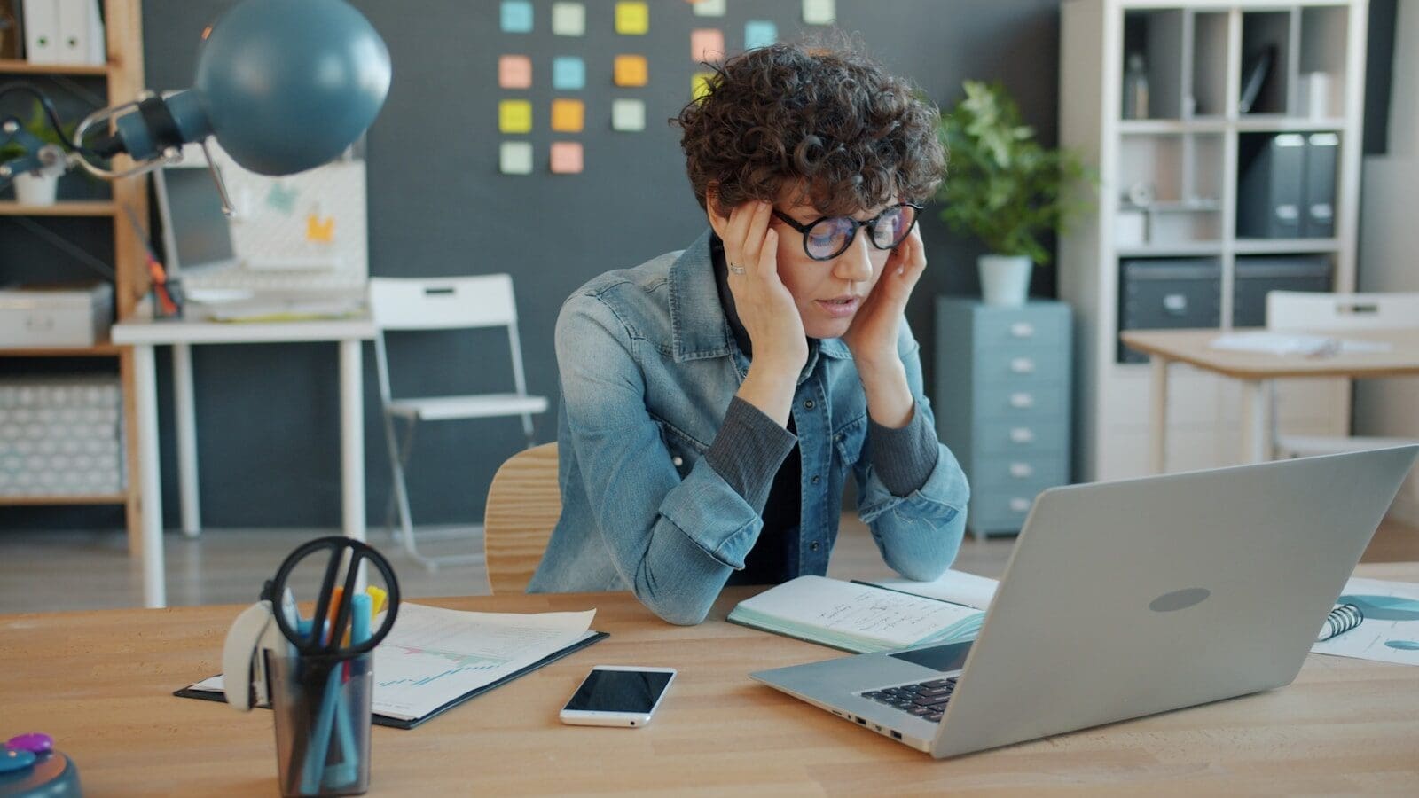A woman lwith glasses looking stressed at a laptop in an office. Is it work stress or a symptom of perimenopause?