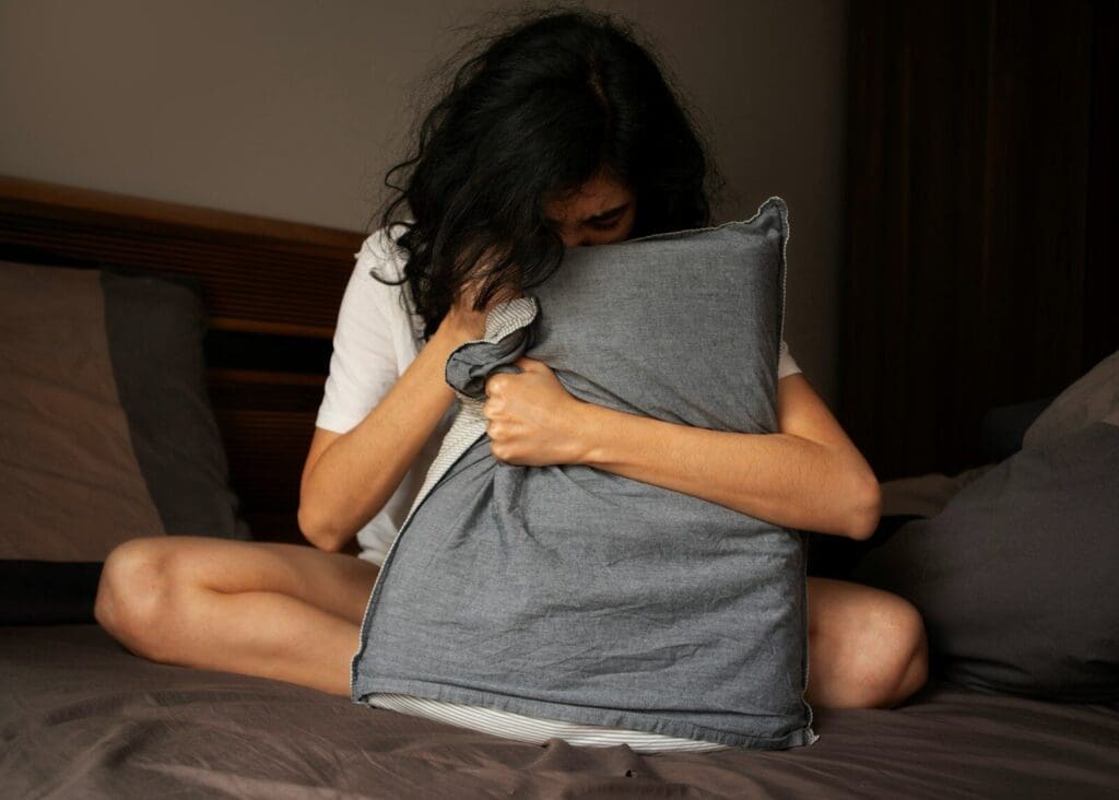 A woman sitting on a bed holding a pillow. Sleeplessness can be a sign of low testosterone.