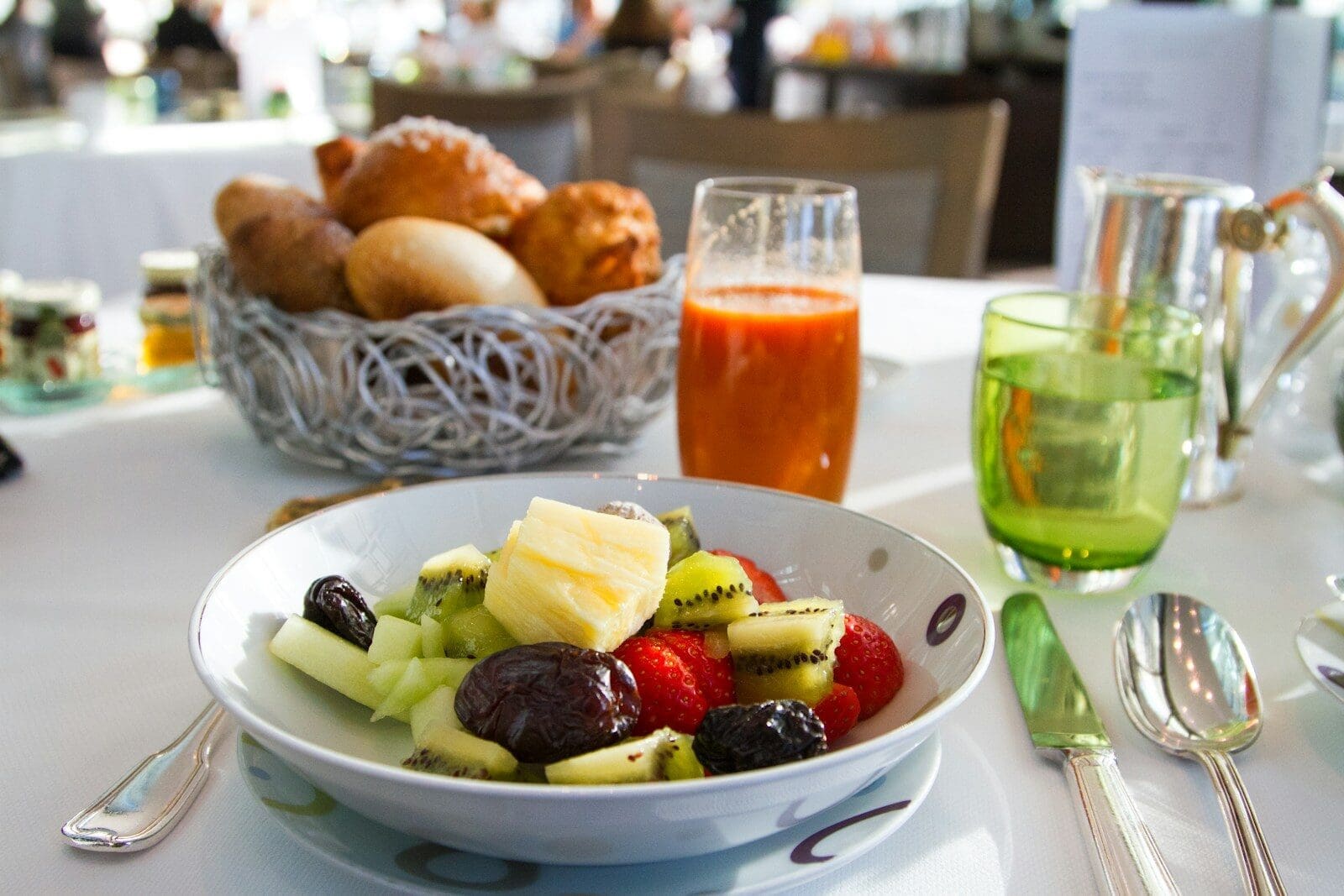 a bowl of fruit including healthy prunes sitting on a table with cutlery and juice