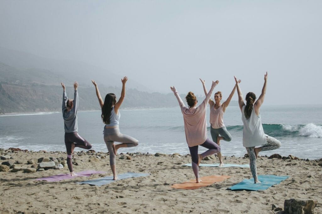 five woman standing on seashore doing yoga. Stress relief id a big part of perimenopause care